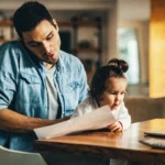 Um pai ocupado atendendo o telefone com a filha no colo.