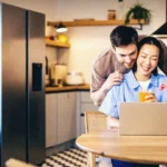 Um casal, um homem branco e uma mulher asiática olhando para o computador e se abraçando.