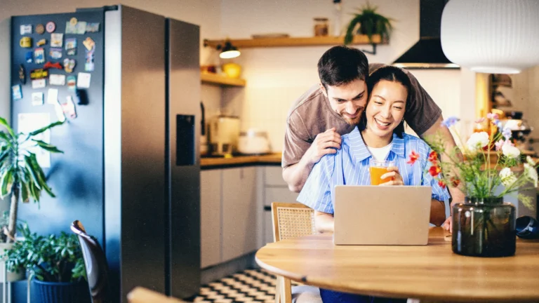 Um casal, um homem branco e uma mulher asiática olhando para o computador e se abraçando.