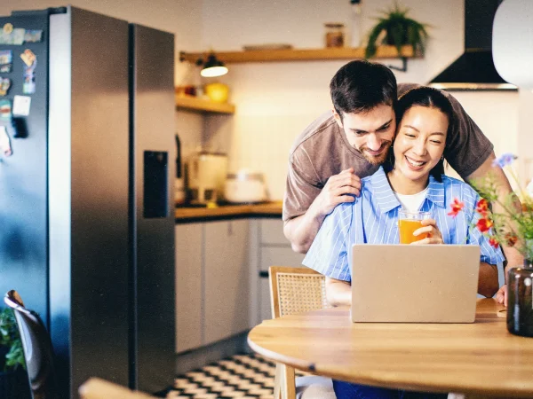 Um casal, um homem branco e uma mulher asiática olhando para o computador e se abraçando.